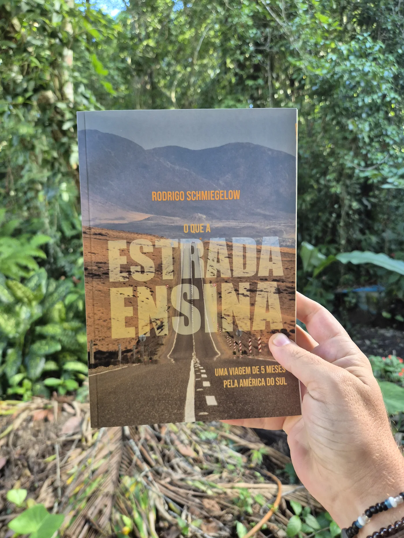 Exemplar do livro O que a Estrada Ensina segurado em frente à mata